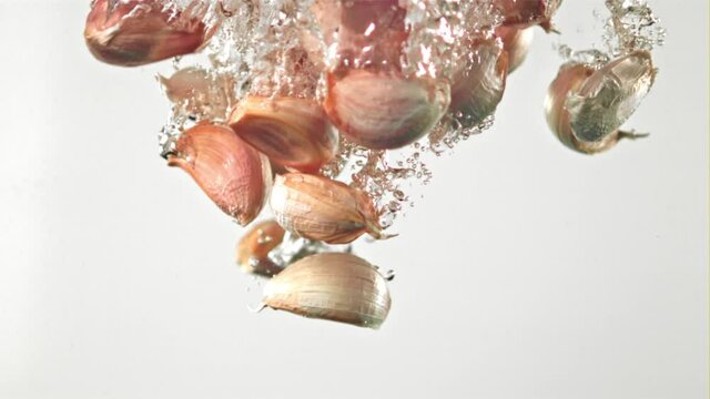 Super slow motion garlic cloves fall under the water on a white background. Filmed on a high-speed camera at 1000 fps. High quality FullHD footage