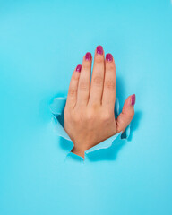 Woman hand in whole of torn blue paper background