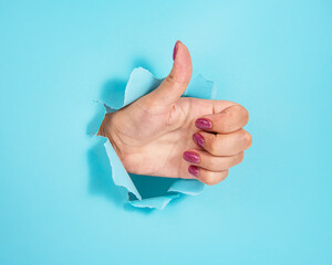 Woman hand in whole of torn blue paper background