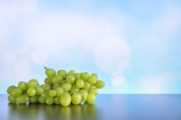 Bunch of green grapes on a table with reflection on a blue bokeh background. Soft selective focus....
