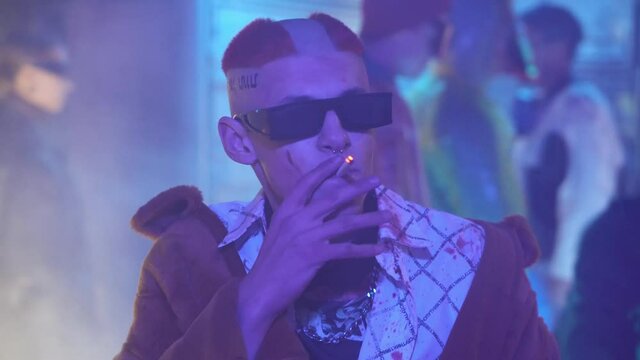 Cyberpunk future concept. Strange character with punk-type haircut lights up and smokes cigarette in night city with neon lighting. Criminal bandit. Science fiction scene, fantasy. World of tomorrow