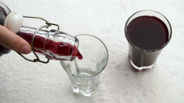 Pouring homemade black elder syrup from a bottle into a glass