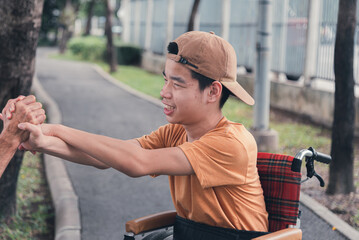 Asian happy disabled teenage boy on wheelchair smiling face with arm muscle strength test with parent, Male style play in teen and lifestyle of diverse family.