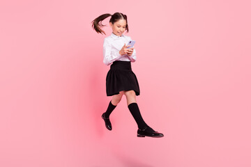 Full size photo of young little brunette tails haired girl jump hold phone walk wear formalwear uniform isolated on pink color background