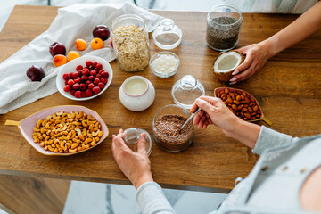 Different ingredients for cooking cereal breakfast on the table. Close up of two women hands cooking together at kitchen.