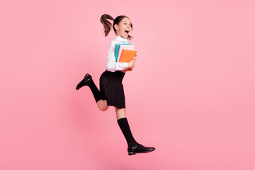 Full body photo of cheerful happy small brunette girl jump look empty space crazy copybook isolated on pink color background