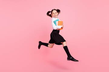 Fototapeta na wymiar Full length photo of young cheerful small girl jump up hold copybooks smile long socks isolated on pink color background
