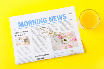 Newspaper with eyeglasses and orange juice on color background
