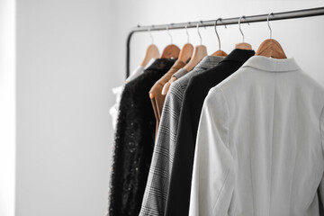 Rack with stylish clothes near light wall