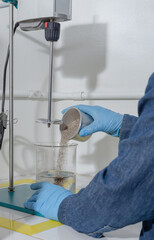 Industrial worker hands with blue latex gloves in test laboratory poring sand in a jar with water