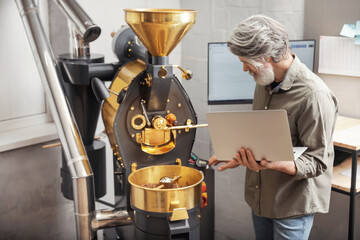 Obraz premium Senior man with laptop using modern coffee roaster