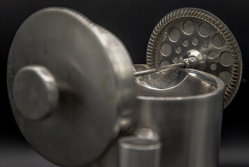 Close-up of Cafetiere plunger is placed on stainless steel jug  with a shallow depth of field on black background.French press coffee. Abstract metalwork of Cafetiere like a weightlifter. Selective fo