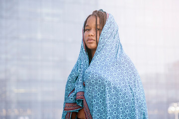 Black Muslim girl, wearing hijab, looking at the camera with a dramatic expression. With a office buildings background. Adolescents, muslims, students, integration, equality and future concept. - obrazy, fototapety, plakaty