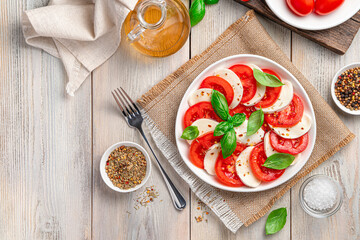 Italian caprese salad with sliced tomatoes, mozzarella cheese, olive oil and basil on a beige wooden background.