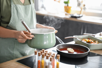 Woman with cooking pot of tasty soup in kitchen