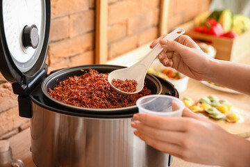 Woman preparing rice in multi cooker at  kitchen table