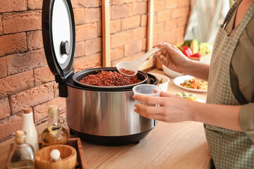 Woman preparing rice in multi cooker at  kitchen table