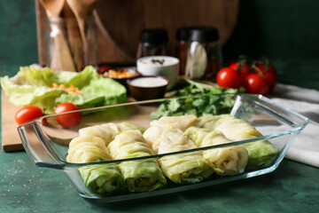 Baking dish with uncooked cabbage rolls on color background