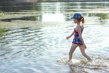 a girl in a swimsuit walks along the river bank on a sunny day,beach family vacation by the river