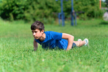 Naklejka na ściany i meble teenage boy exercising outdoors, sports ground in the yard, he does push-ups on the green grass field, healthy lifestyle