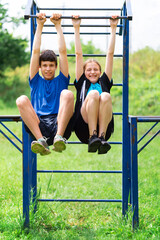 Fototapeta premium teenage boy and girl exercising outdoors, sports ground in the yard, they posing at the horizontal bar, healthy lifestyle
