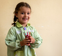 Adorable niña en su primer día de colegio  vestida con mandilón a cuadros verdes dibujando y...