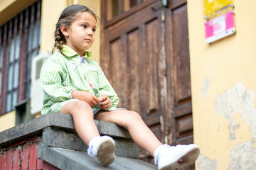 Adorable niña en su primer día de colegio  vestida con mandilón a cuadros verdes dibujando y...