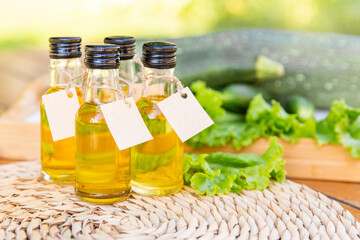Four types of vegetable oil in small bottles with cardboard labels on the background of salad leaves, zucchini and cucumbers. The concept of healthy healthy food.