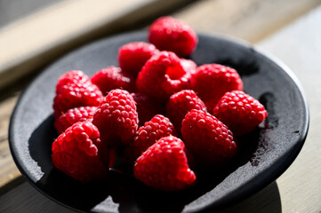 Raspberries in a plate backlit by the sun.