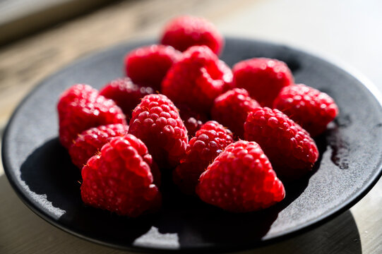 Raspberries in a plate backlit by the sun.