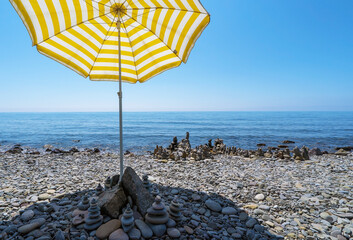 An umbrella from the sun creates shade on a pebble beach . The Black Sea coast of Crimea.