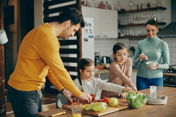Happy small girls and their parents make salad in the kitchen.