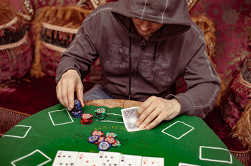 A suspicious man with a hood on the face plays a poker card in an expensive casino interior