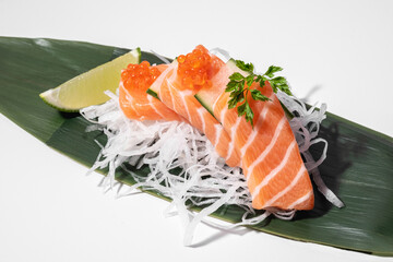 Salmon sashimi on white background. Traditional Japanese food. Raw salmon fish served with red trout caviar, decor, daikon and lime on bamboo leaf. Sushi restaurant menu. Copy space, close up