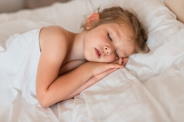 Adorable little girl sleeping in bed with white linens. Place for your text. Healthy baby sleep.