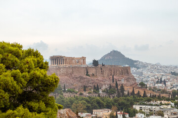 Fototapeta na wymiar Acropolis (Parthenon, Temples), Mount Lycabettus and white city buildings with vivid pine summer greenery. Athens ancient historical landmark from Filopappou Hill on cloudy day
