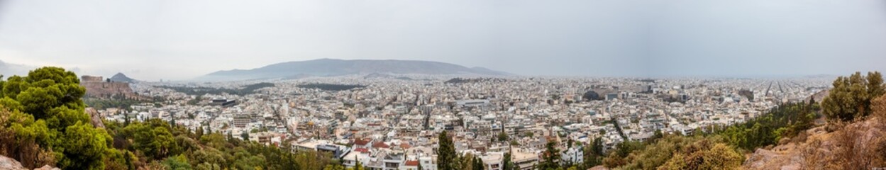Fototapeta na wymiar Wide panorama on Athens city center with white architecture buildings, Acropolis and mountains in vivid greenery on cloudy dramatic day from Filopappou Hill