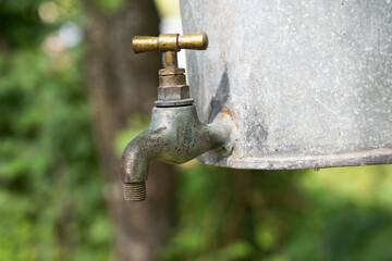 An old vintage water faucet is attached to a galvanized garden sink. There is an aged gray metal...