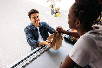 Young smiling man receiving a meal from a saleswoman. Male buying takeaway food.