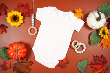 Autumn theme white baby romper onesie jumpsuit mockup flatlay on brown tan background with autumn...