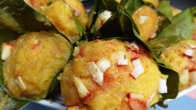 Traditional steamed ripe palmyra palm fruit cake wrapped with jackfruit leaves and sprinkled with coconut pieces. Steamed palmyra palm cake in closeup view. 4k video.