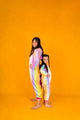 two girls in plush pajamas stand on a yellow background with a place for text