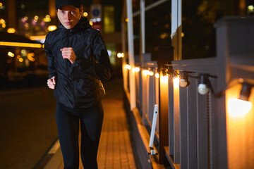 young caucasian woman running by night in city street. Fitness and workout wellness concept. Sports outdoors. Garlands are lighting the street in the night, outdoor sport concept. copy space