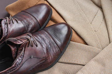 Flat lay of men dark brown derby shoes combined with light beige blazer and brown sweater and belt.