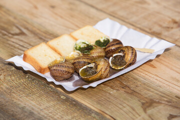 Cooked snails with butter, herbs and toast bread on a wooden table.