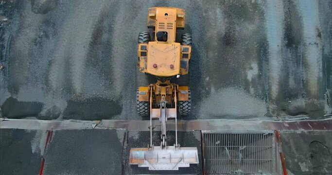 Loader unloads the asphalt from the bucket into a hopper or container. Unloading of asphalt to the construction base. Construction works. View from a quadrocopter. 4k, ProRes