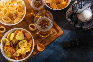 A traditional set of sports fans - glasses of beer, chips, snacks, onion rings. A baseball glove and a TV remote control are on the table nearby. Watching a sports match on TV. hobby, relaxation...