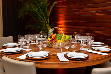 table set for dinner with white plates, glass glasses and alcohol to sanitize hands, ornamental flowers