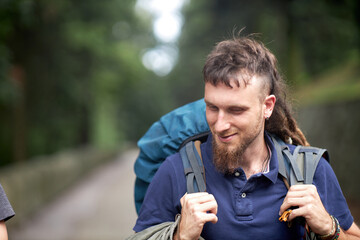 Camping and having fun: a young alternative hippie man walking through the mountain or forest, carrying a big rucksack - backpack on his back, going away for a vacation