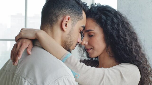 Multiracial multiethnic spanish couple married newlyweds caucasian brunette wife and hispanic man husband standing embracing hugging cuddling forehead touching with close eyes enjoy tenderness love